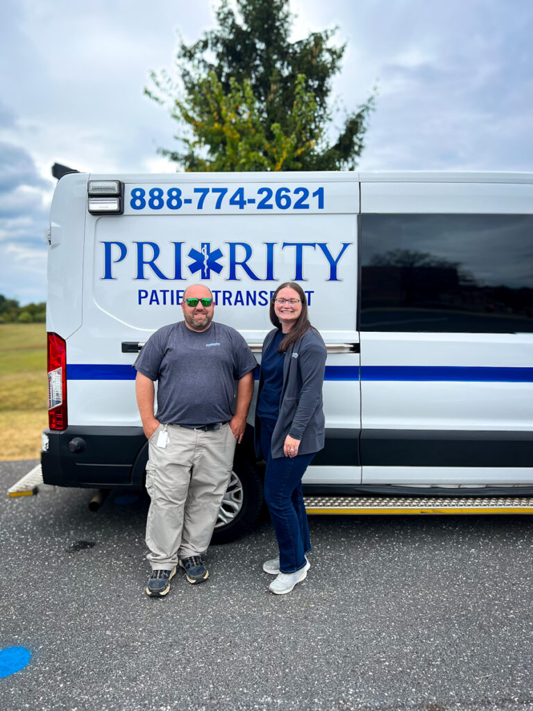 Two Priority team members standing in front of a Priority Patient Transport van